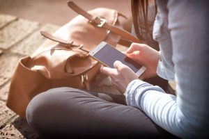 Woman is travelling and sitting on the ground with her bag, reading on her phone